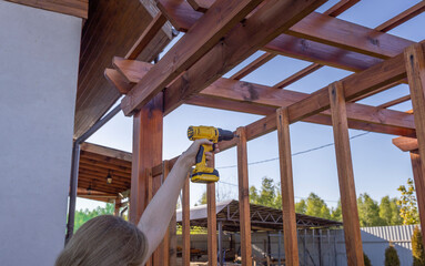 A screwdriver close-up, it is held by a woman&acirc;&euro;&trade;s hand, against the background of the sky, the process of screwing the slats to a wooden structure, working in the garden.