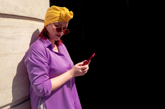 Happy and funny cool lady with fashionable clothes on dark background look to the phone seriously and thoughtfully - adult asian with extravagant style isolated on black background