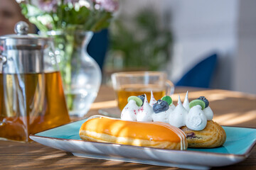 Close-up of a cream puff on a blue plate, with teapot and teacup in a cozy café with soft light.