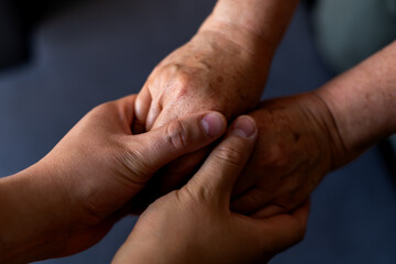 Fototapeta premium Close-up of an adult son and his elderly mother holding hands, conveying a sense of support, love, and connection