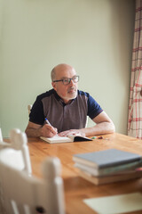 Fototapeta premium Elderly man relaxing at home, reading on an armchair at home clothes