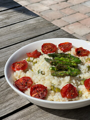 Risotto with asparagus and cherry tomatoes on wooden table. Close up.