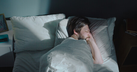 Beautiful Caucasian man sleeping at night after exhausting day. Young male yawns and covers with a...