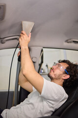 Man is using a vacuum cleaner and wearing protective goggles while cleaning the interior of a car