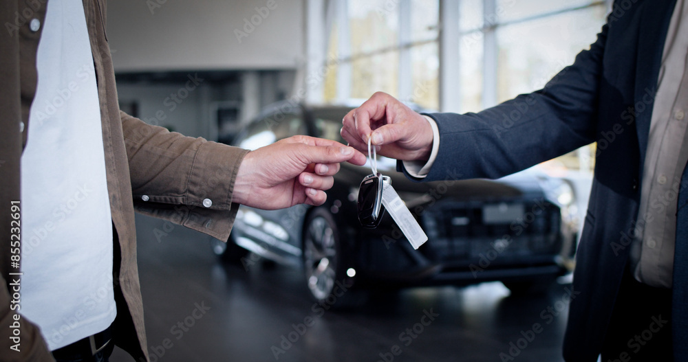 Wall mural male hand gives a car keys to male hand in the car dealership close up. unrecognized auto seller and