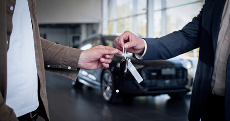 Male hand gives a car keys to male hand in the car dealership close up. Unrecognized auto seller...