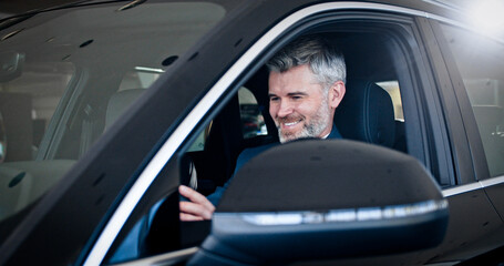 Smiling caucasian man touching steering wheel and looking around inside automobile. Successful businessman choosing vehicle in car dealership. Side view, close-up.