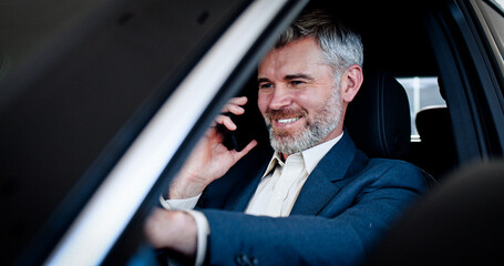 Smiling caucasian businessman talking on phone, touching steering wheel and looking around inside automobile. Successful young bearded man buy vehicle in car dealership. Close-up.