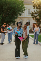 Full length of happy diverse college girls with books posing at campus