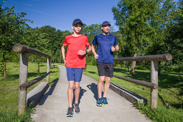 Fototapeta premium Father and son run together along a path in the park.