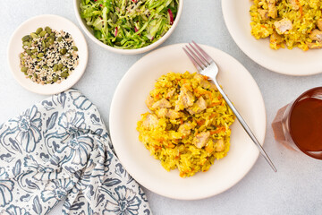 Stewed rice with chicken breast and mixed salad with radishes and various seeds, a served table with food and a vase of flowers, a delicious hearty lunch or dinner