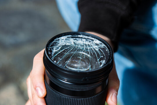Hands of young photographer holding DSLR photo camera with  broken lens filter glass after if fall down onto the floor. Close up. Destroyed cracked photo-filter. Macro. Top view. Selective focus. - Powered by Adobe