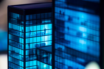 A close-up shot of a miniature office building model with blue lights illuminating the windows. The...