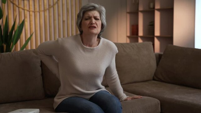 Elderly woman getting up from a couch. She appears to be experiencing back pain.