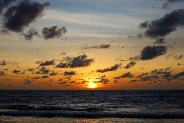 Naklejka premium Sunrise on a beach, orange sun is shining through the dark clouds. Sea background for romantic travel