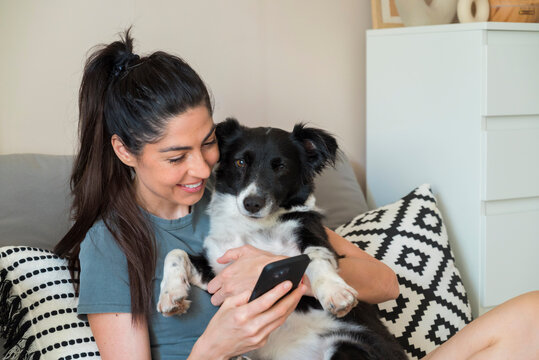 Beautiful  young woman sitting at home ,hugging her adopted dog and  using mobile phone
