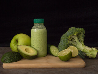 Green smoothie in bottle, surrounded by fresh avocado, lime, broccoli, apple, cucumber Perfect smoothie for health and wellness content Highlighting ingredients for nutritious and refreshing smoothie.