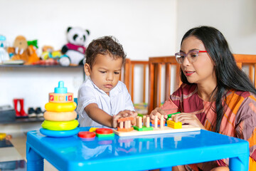 Son focused while playing at home with his young mother, both are Latino, and many toys are seen in...