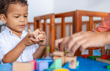 A child playing with wooden blocks with different patterns and colors, he is interested in the toy and learning at the same time next to his mother. Both, Latinos, are at home