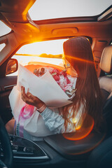 Naklejka premium Girl with a large bouquet of peonies in a car at sunset