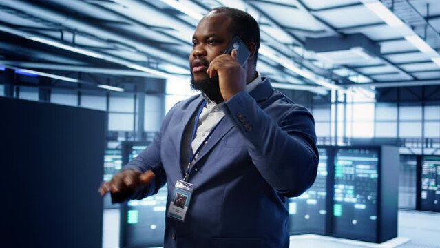 IT support worker in data center talking in phone call, doing yearly checkup. On field engineer chatting with manager in server hub during telephone call, monitoring servers infrastructure, camera B