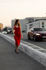 Beautiful self confident young woman in a red dress walking down the street. Urban cityscape. Concept of freedom, feminism, female strength. Summer, sunset light