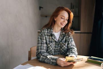 Cheerful young housewife content with savings, counts money joyfully, secure and happy with financial stability. Joyful female satisfied of income and saves money for planned vacation, gifts.