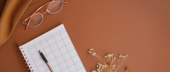 Stylish feminine home office desk setup with weekly planner, pen, keyboard, silk, glasses, stationery, and dried flowers on beige background. Flat lay, top view.