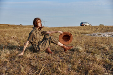 Woman sitting in field with hat on head and car in background a serene moment of travel and nature beauty