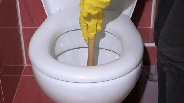 Working with plunger in toilet bowl. A lady hands working in gloves with plunger by the toilet bowl during daily work indoor.