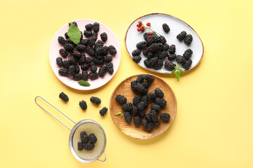 Plates with fresh blackberries on yellow background