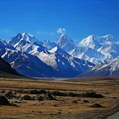 Fototapeta premium Breathtaking view of snow-capped mountains under a clear blue sky, with a vast valley in the foreground. Perfect for nature and landscape themes.