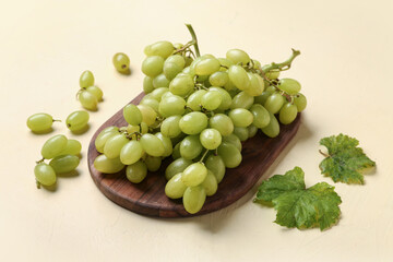 Wooden board with fresh green grapes and leaves on color background
