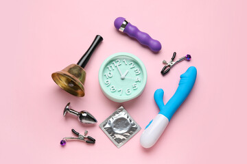Alarm clock with sex toys, bell and condom on pink background