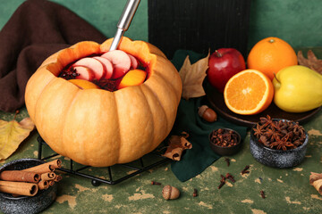 Beautiful composition with tasty mulled wine in pumpkin on green background