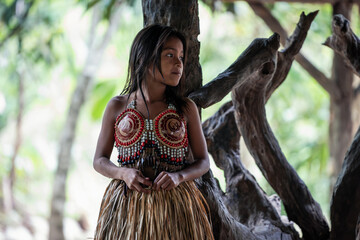 Wayuri indigenous girl in traditional dress gazes right leaning against tree in Ecuadorian jungle