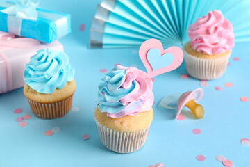 Delicious cupcakes with gift boxes, pacifier and decor on blue background. Gender reveal party concept