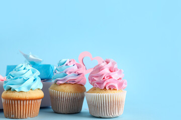 Delicious cupcakes with gift boxes on blue background. Gender reveal party concept