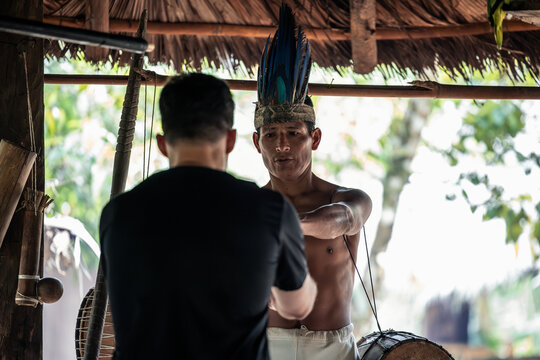 Indigenous Wayuri tribe member presents shamanic drum to tourist in Ecuadorian jungle
