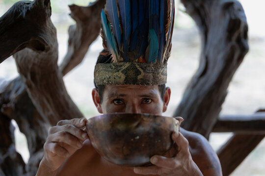 Indigenous Wayuri Man Drinking Chicha from Bowl Wearing Feather Crown in Puyo, Ecuador