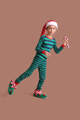 Cute little boy in Christmas pajamas with candy cane toy on brown background
