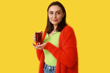 Beautiful young woman with glass cup of hot mulled wine on yellow background