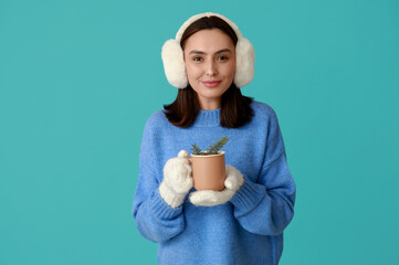 Beautiful young woman in warm mittens with cup of hot mulled wine on blue background