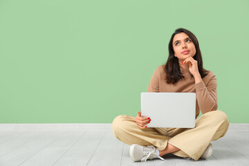 Thoughtful young woman with laptop sitting near green wall. Online dating concept