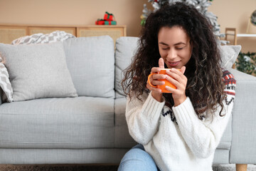 Beautiful young African-American woman with cup of hot mulled wine at home