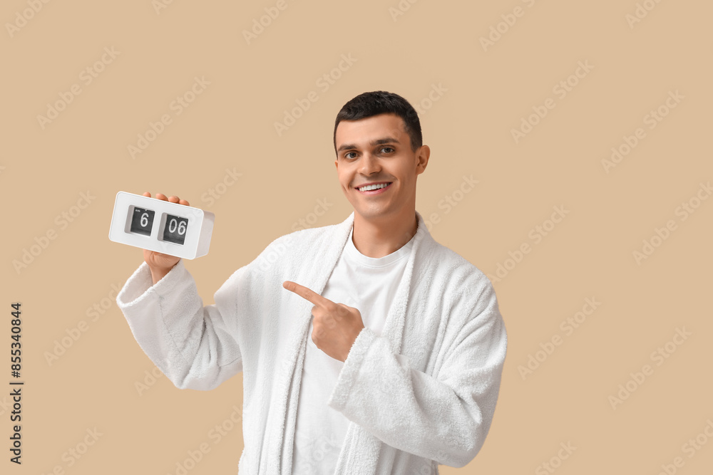 Canvas Prints Portrait of handsome young man in bathrobe with clock on beige background