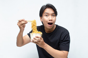 young Asian man enjoys his noodles with deep pleasure using chopstick and paper bowl. man in black tshirt eats noodles with great enthusiasm.