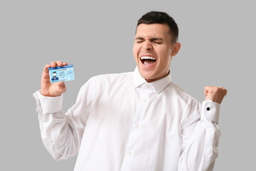 Young happy man with driver license on grey background