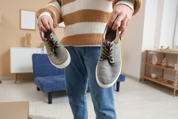 Young man holding stylish shoes at home