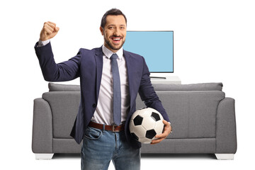 Cheerful man holding a football and gesturing win in front of a tv and couch